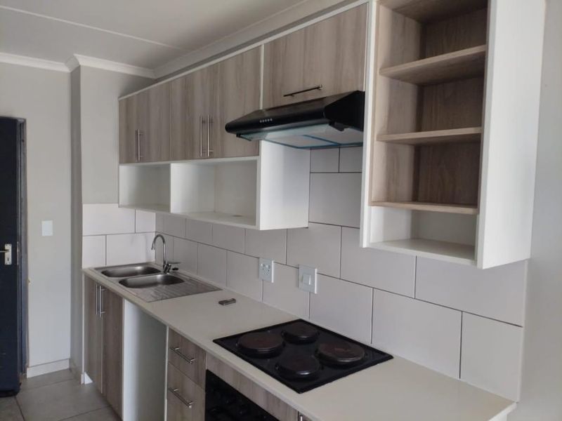 Modern kitchen featuring light wood-tone cabinetry, subway tile backsplash, integrated electric hob, extractor fan, and a stainless steel double sink.