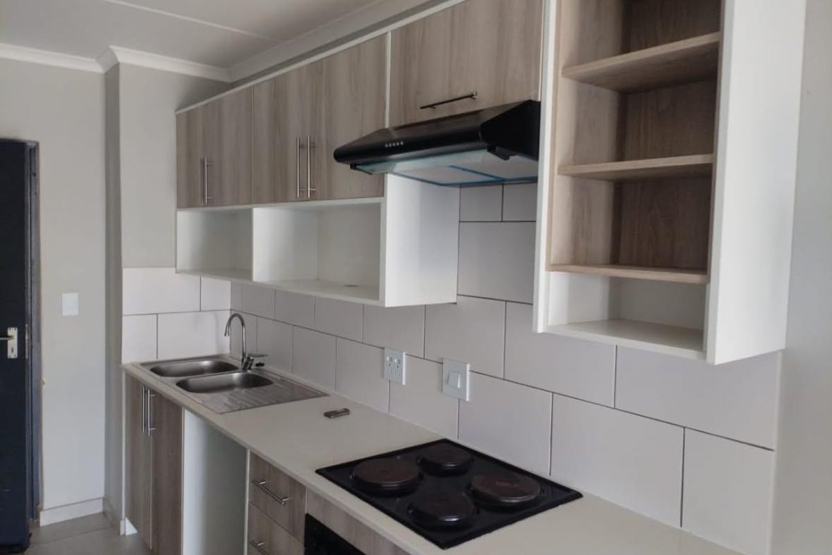 Modern kitchen featuring light wood-tone cabinetry, subway tile backsplash, integrated electric hob, extractor fan, and a stainless steel double sink.