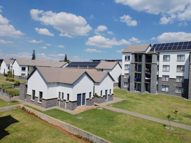 Aerial view of a modern apartment complex featuring stone-clad facades, tiled roofs with integrated solar panels, and well-maintained communal garden areas.