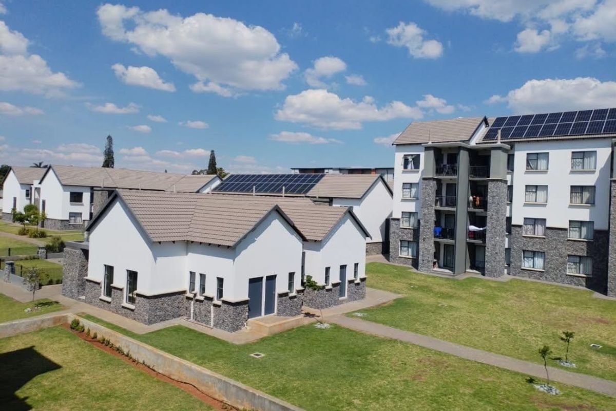 Aerial view of a modern apartment complex featuring stone-clad facades, tiled roofs with integrated solar panels, and well-maintained communal garden areas.