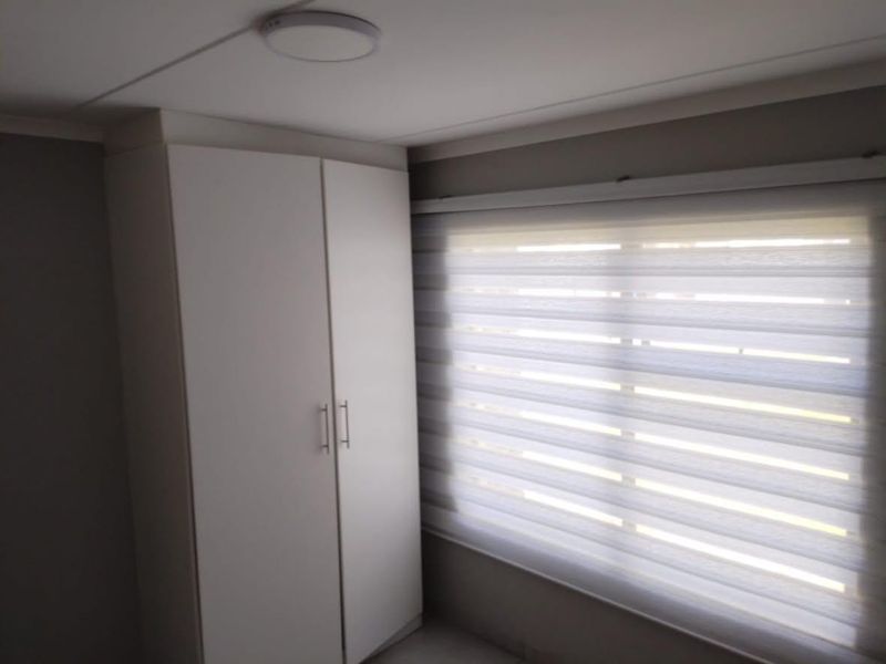 A clean bedroom featuring a built-in white wardrobe and modern zebra blinds, providing a neutral and functional space.