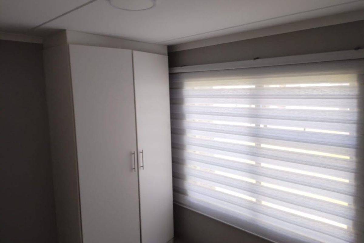 A clean bedroom featuring a built-in white wardrobe and modern zebra blinds, providing a neutral and functional space.