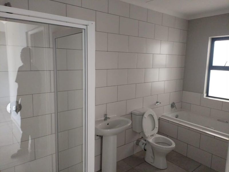 A clean, modern bathroom featuring a pedestal basin, toilet, built-in bathtub, and a separate shower enclosure with neutral wall tiling.