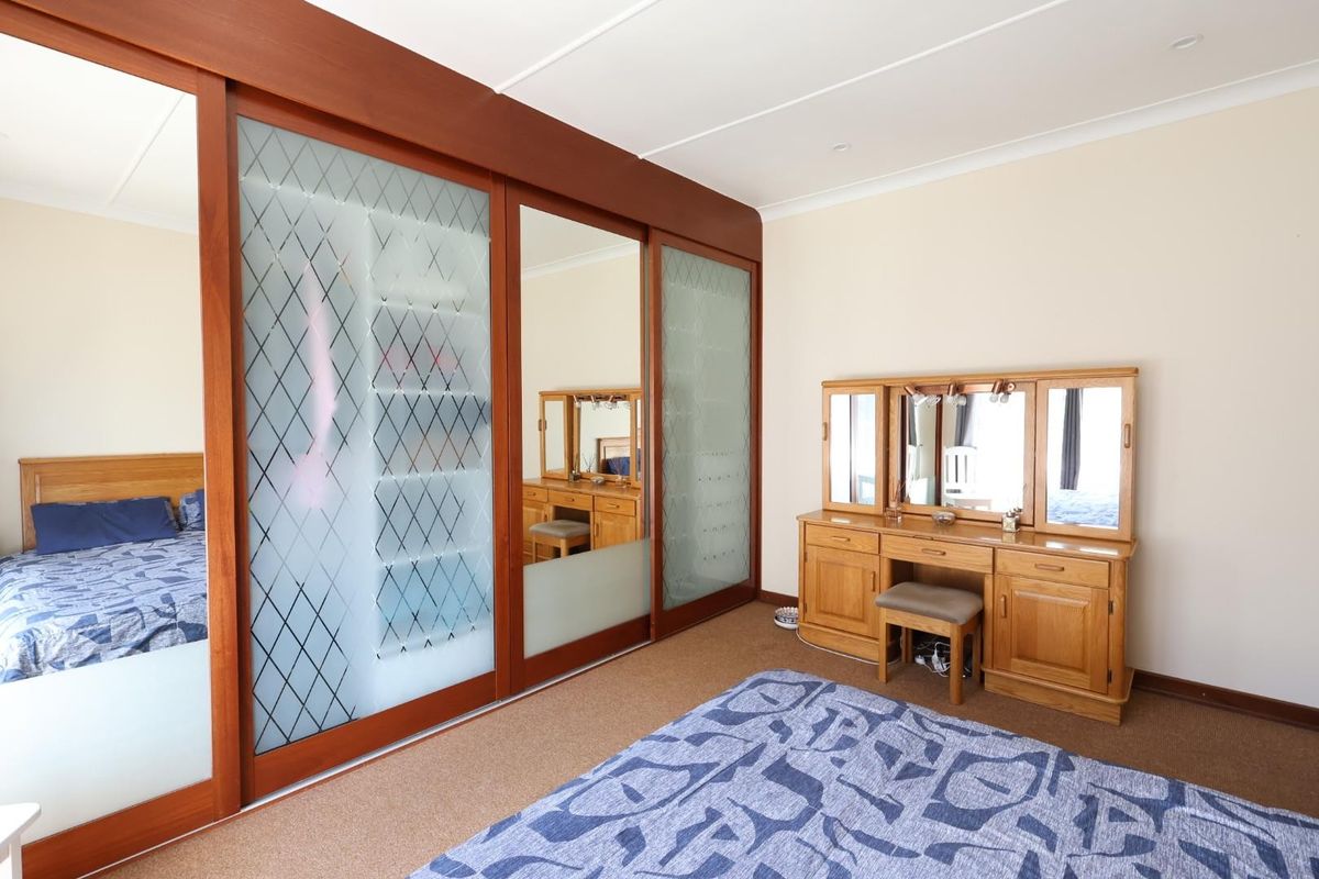 A bedroom featuring a large built-in wardrobe with sliding frosted glass and mirror panels, neutral walls, and carpeted flooring.