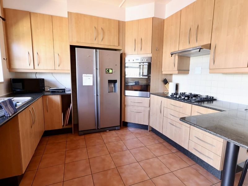 Functional kitchen featuring light wood cabinetry, granite countertops, a gas hob, built-in oven, and tiled flooring with a practical layout.