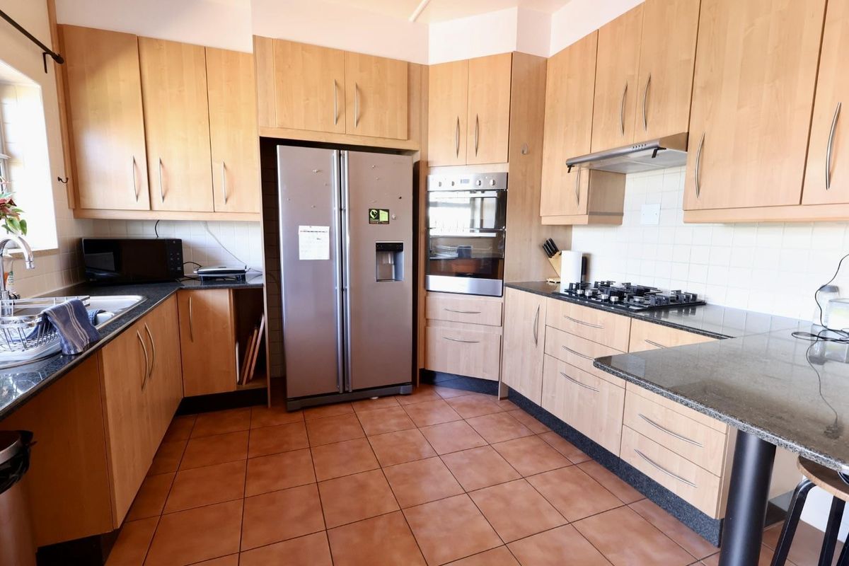 Functional kitchen featuring light wood cabinetry, granite countertops, a gas hob, built-in oven, and tiled flooring with a practical layout.