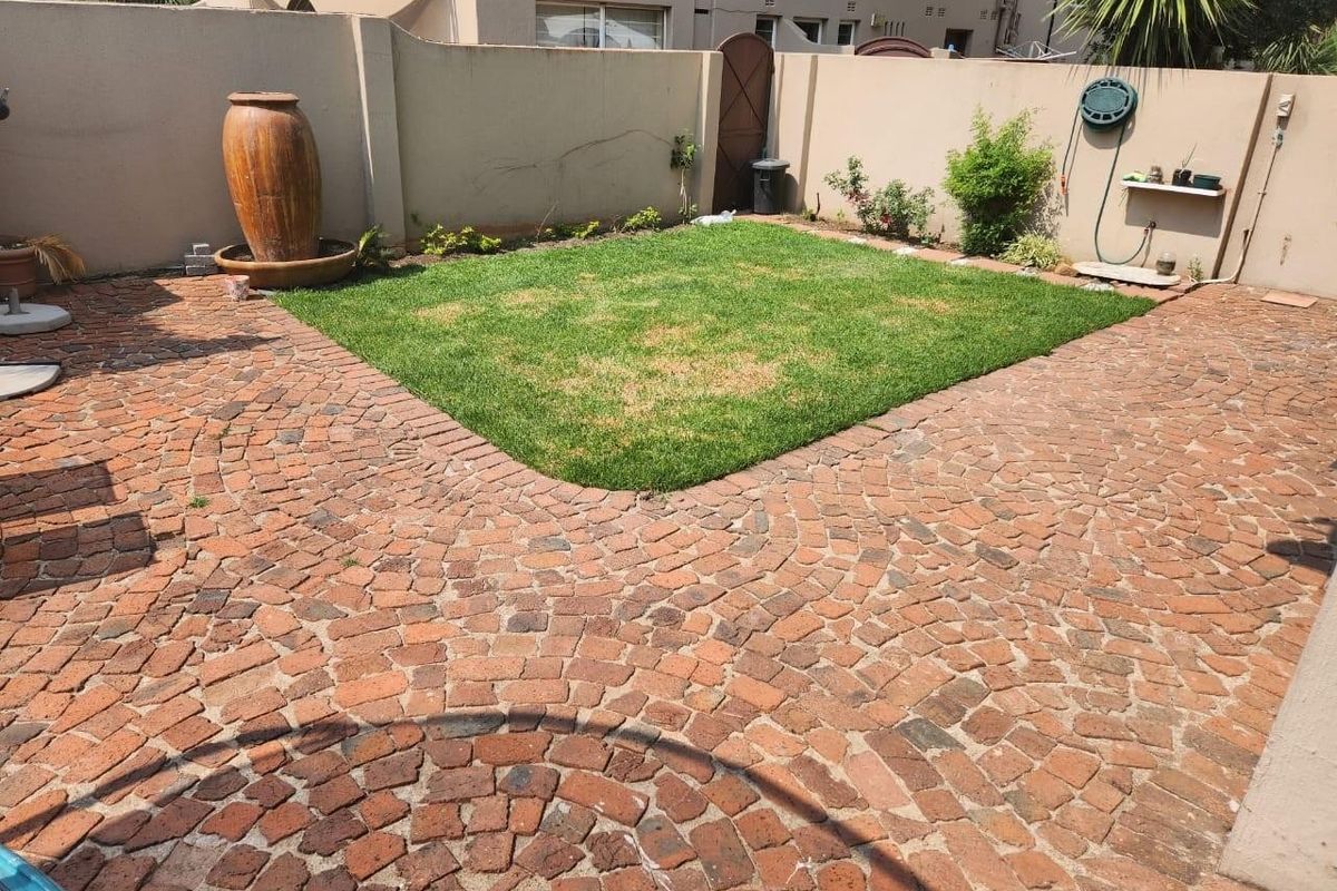 A private rear garden featuring a central lawn area surrounded by classic brick paving and a high boundary wall for privacy.