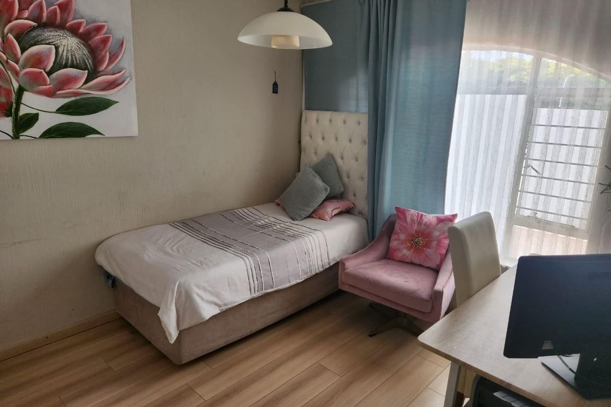 A functional bedroom featuring laminate flooring, neutral wall finishes, and a large window with curtain tracks, providing a comfortable living space.