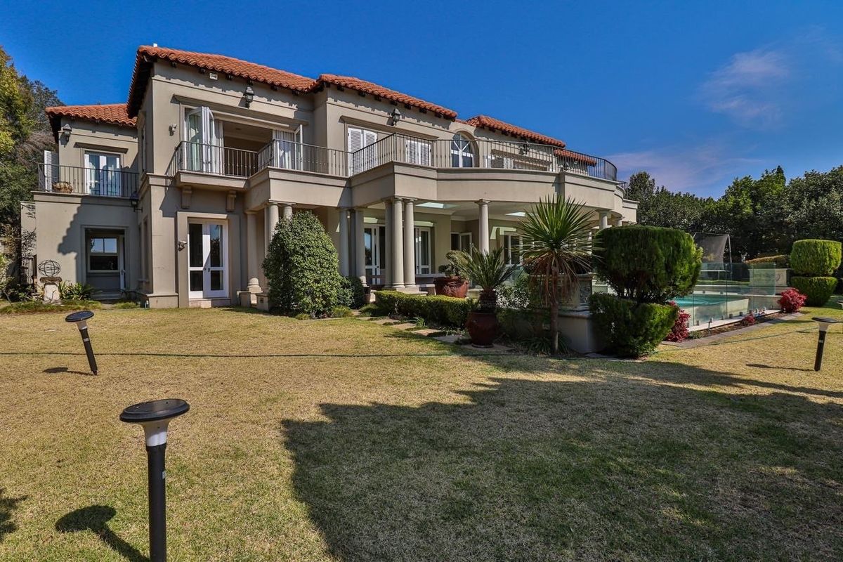 Rear view of a double-story residence featuring a covered patio, upper-level balcony, swimming pool with glass fencing, and a well-maintained garden.