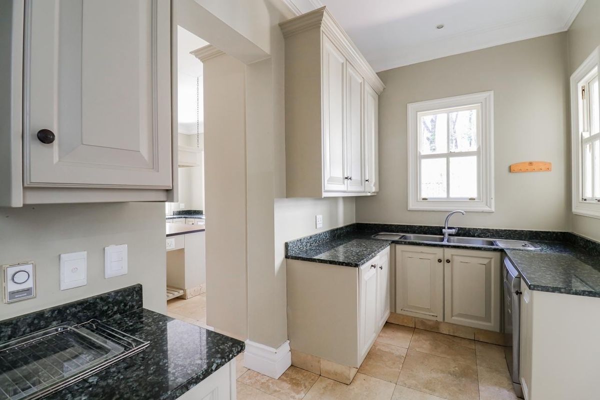 A clean, well-maintained kitchen featuring granite countertops, shaker-style cabinetry, and tiled flooring, with an adjacent scullery area visible through the doorway.
