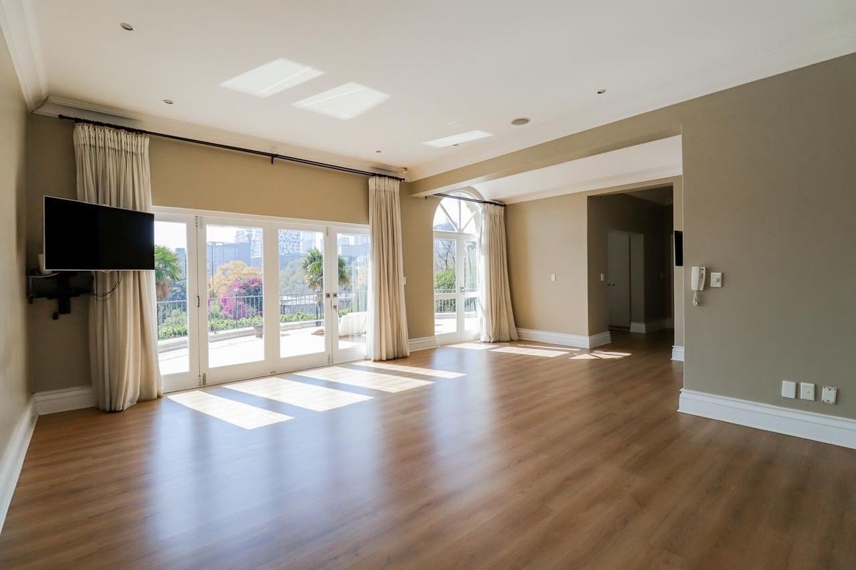Spacious, light-filled living area featuring laminate flooring, recessed lighting, skylights, and large glass doors opening to an outdoor patio.
