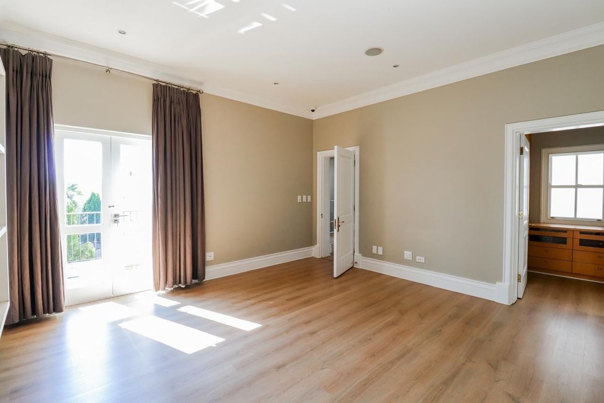 A spacious, light-filled bedroom featuring laminate flooring, recessed lighting, and direct access to a balcony through glass french doors.