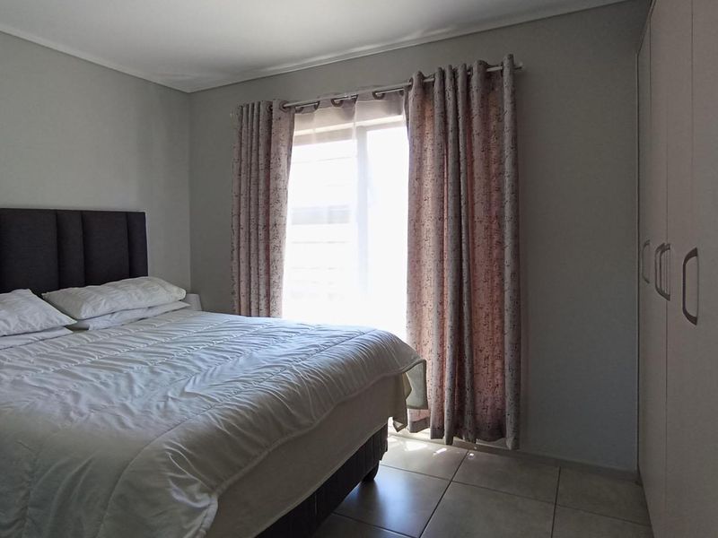 A functional bedroom featuring neutral tiled flooring, built-in storage cupboards, and a sliding door providing natural light.