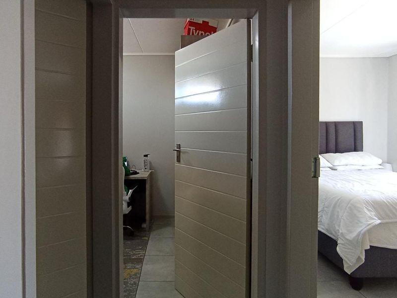 A view from a hallway looking into a bedroom and a small office space, featuring tiled flooring and modern horizontal panel doors.