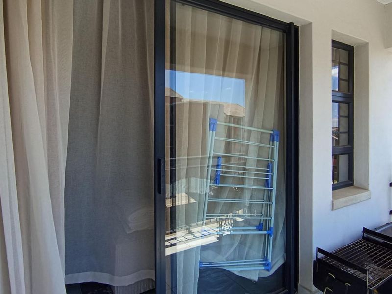 A covered balcony area featuring a sliding glass door, metal balustrade, and a window, providing an outdoor extension to the apartment living space.