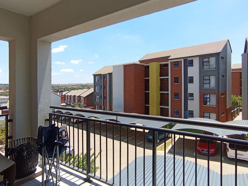 A covered balcony featuring a metal balustrade, offering an elevated view of the apartment complex and parking area.