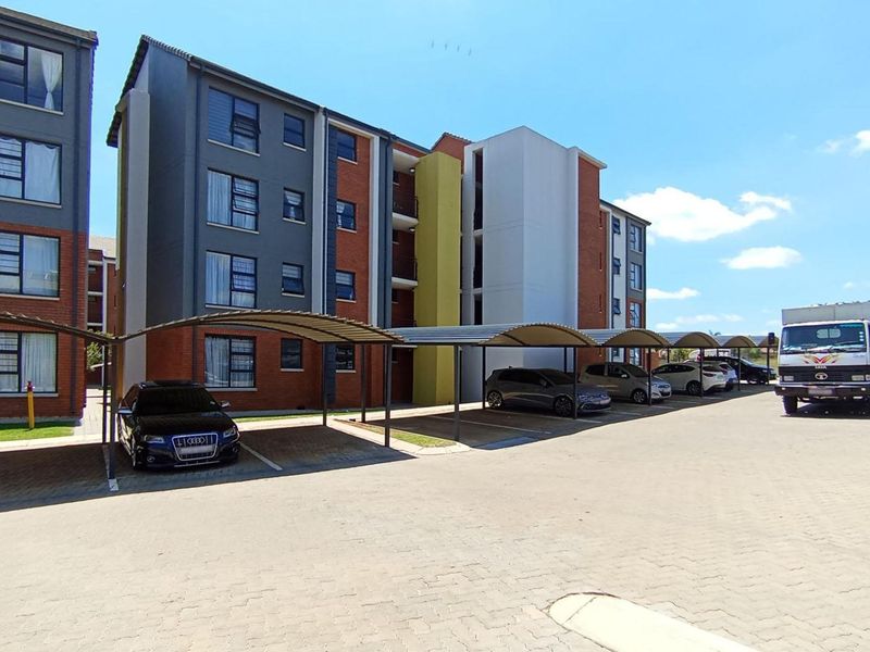 Exterior view of a modern multi-story apartment complex featuring a paved parking area with covered carports.