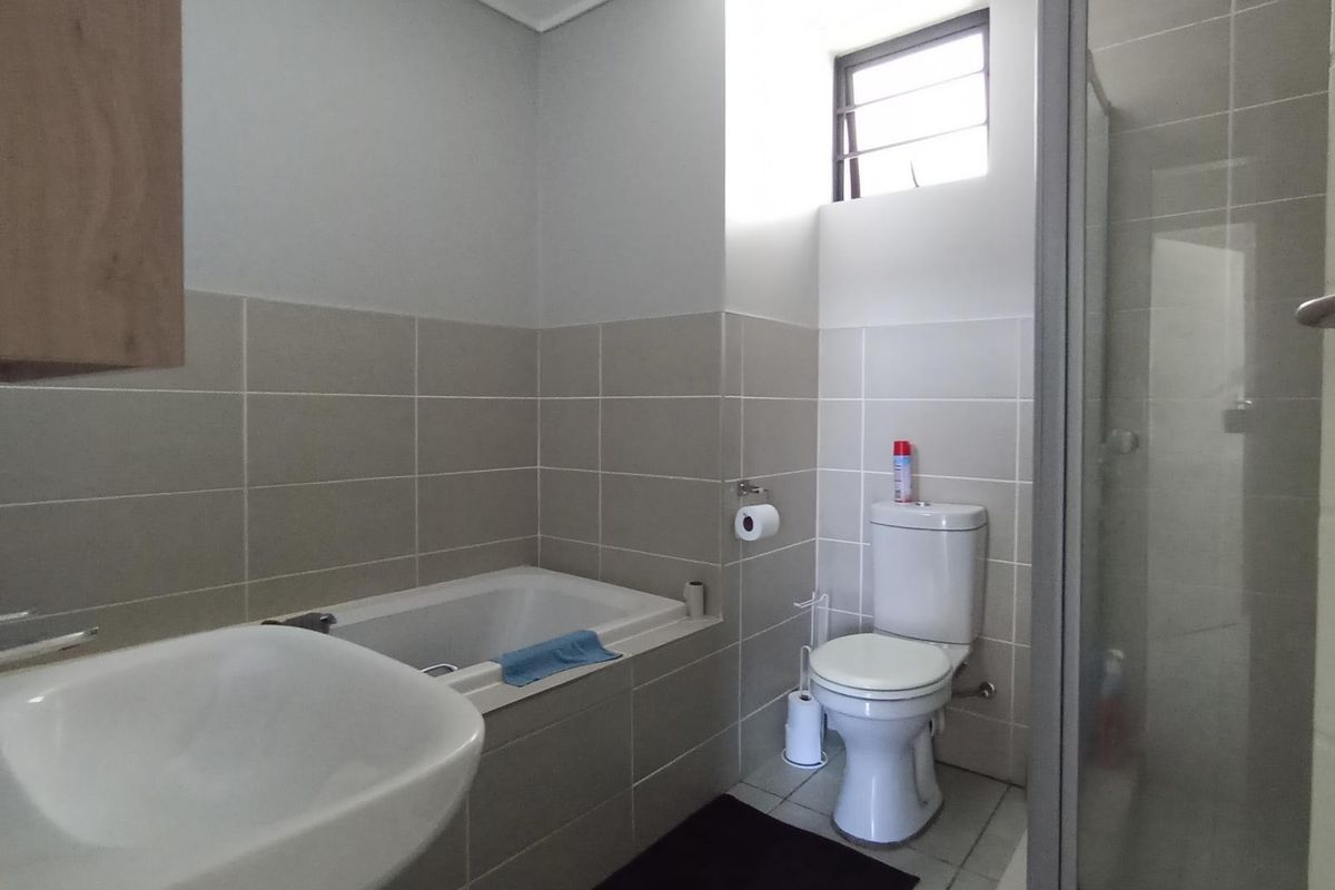 A functional bathroom featuring a built-in bathtub, separate shower enclosure, toilet, and wall-mounted basin with neutral tiled finishes.