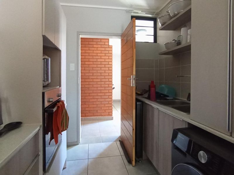 A functional scullery area featuring built-in cabinetry, a stainless steel sink, tiled splashbacks, and a built-in oven, providing additional workspace and storage.