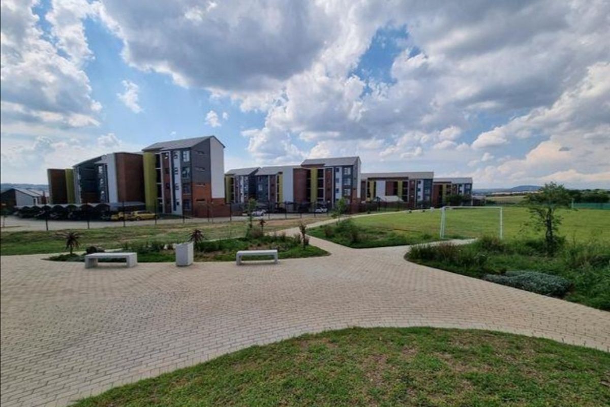 A view of the apartment complex exterior featuring paved walkways, landscaped green spaces, concrete benches, and a recreational area with a soccer goal post.