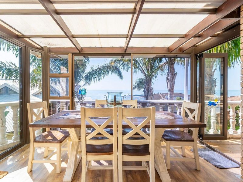Enclosed patio area featuring timber framing, translucent roofing, and expansive glass doors offering scenic coastal views.
