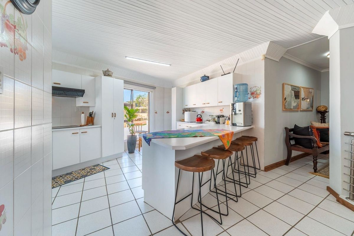 A functional kitchen featuring white cabinetry, a breakfast bar, tiled flooring, and direct access to the outdoor area through a sliding glass door.