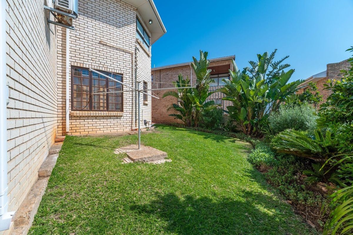 A private rear garden area featuring a brick exterior wall, established greenery, and a fixed rotary clothesline.