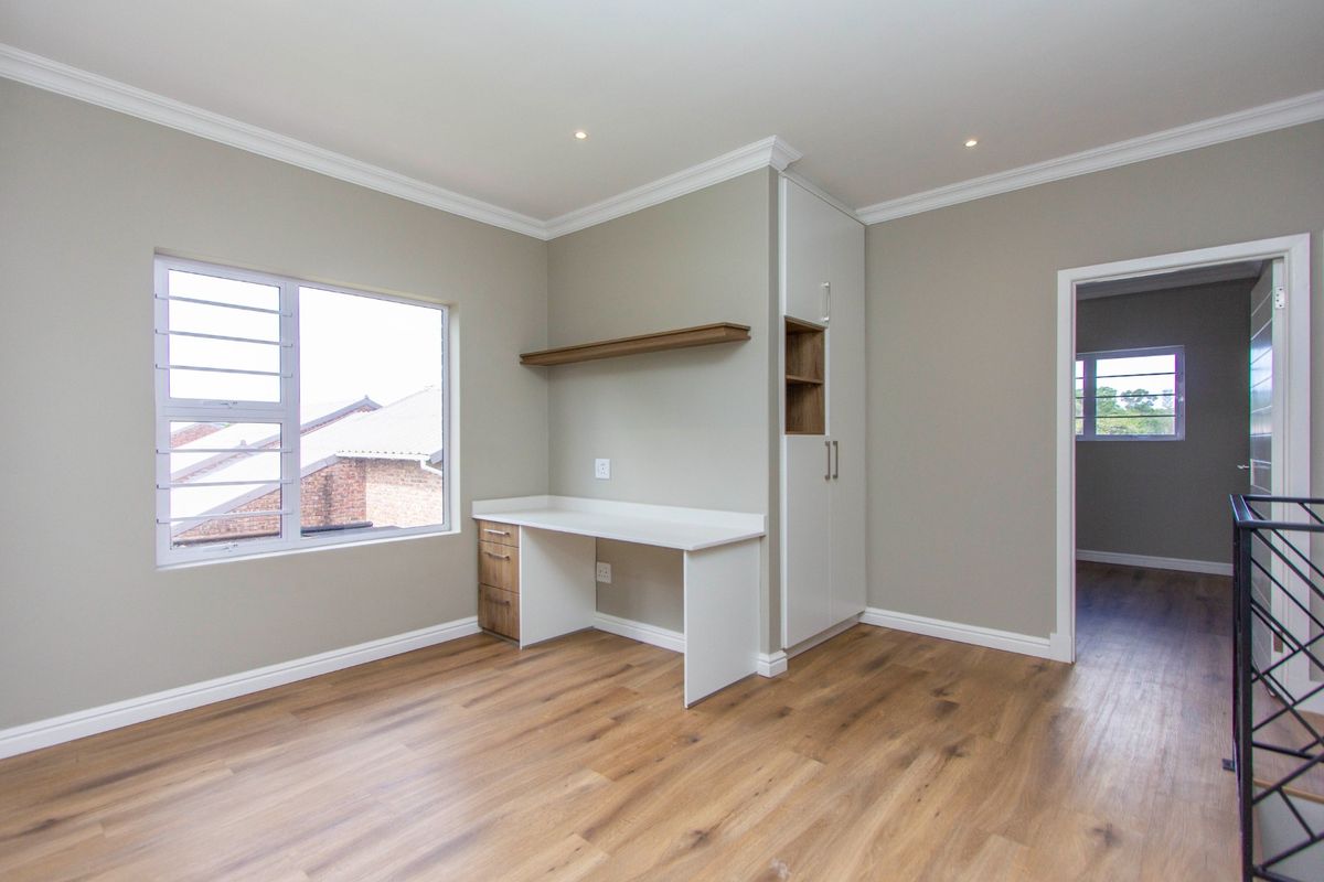 A bright, modern bedroom featuring high-quality laminate flooring, built-in desk and cabinetry, recessed lighting, and crown molding, offering a clean and versatile living space.