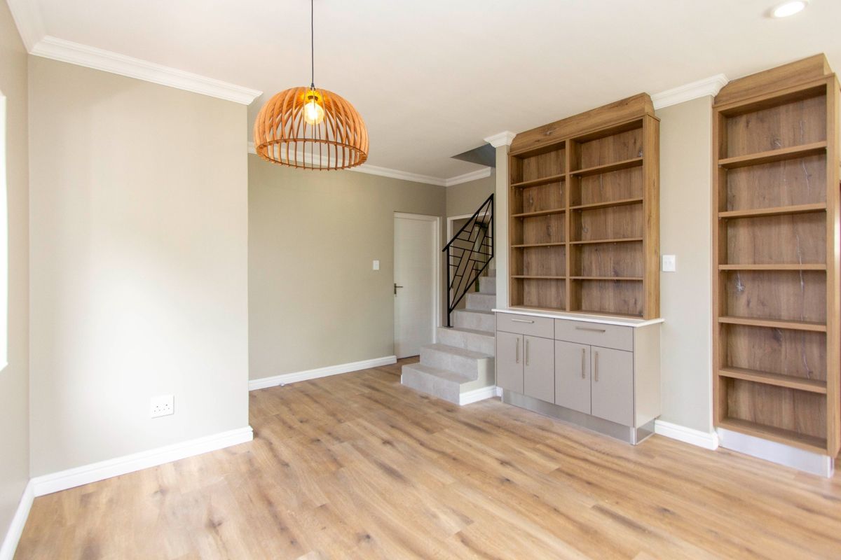 A bright, open living area featuring modern laminate flooring, built-in wooden shelving and cabinetry, and a staircase with a decorative metal balustrade.