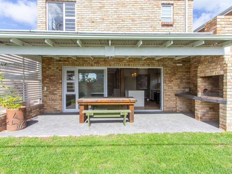 A covered brick patio featuring a built-in braai, paved flooring, and direct access to the interior living space through sliding glass doors.