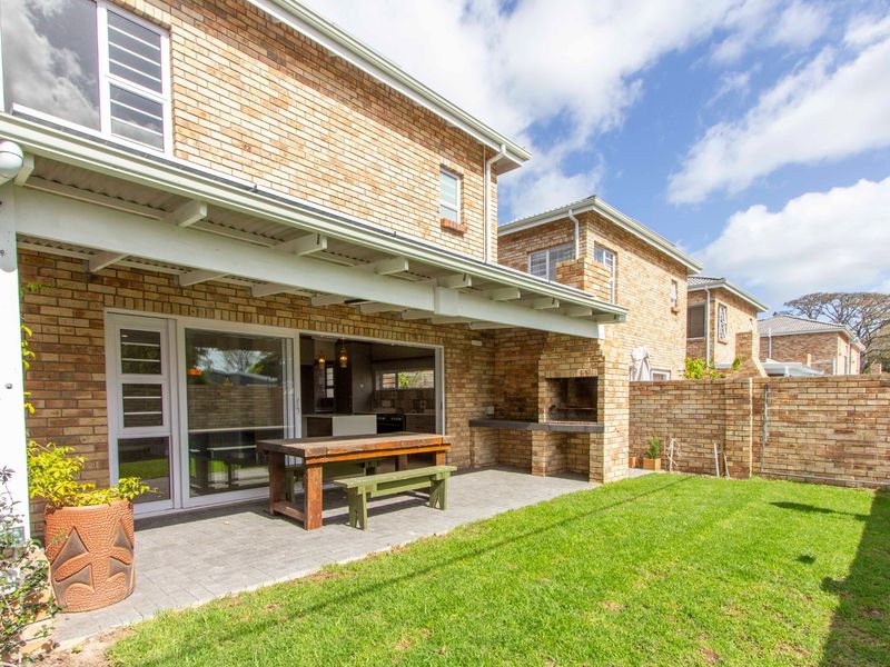 Rear view of the townhouse featuring a covered patio with a built-in braai, paved flooring, and access to the garden through sliding glass doors.
