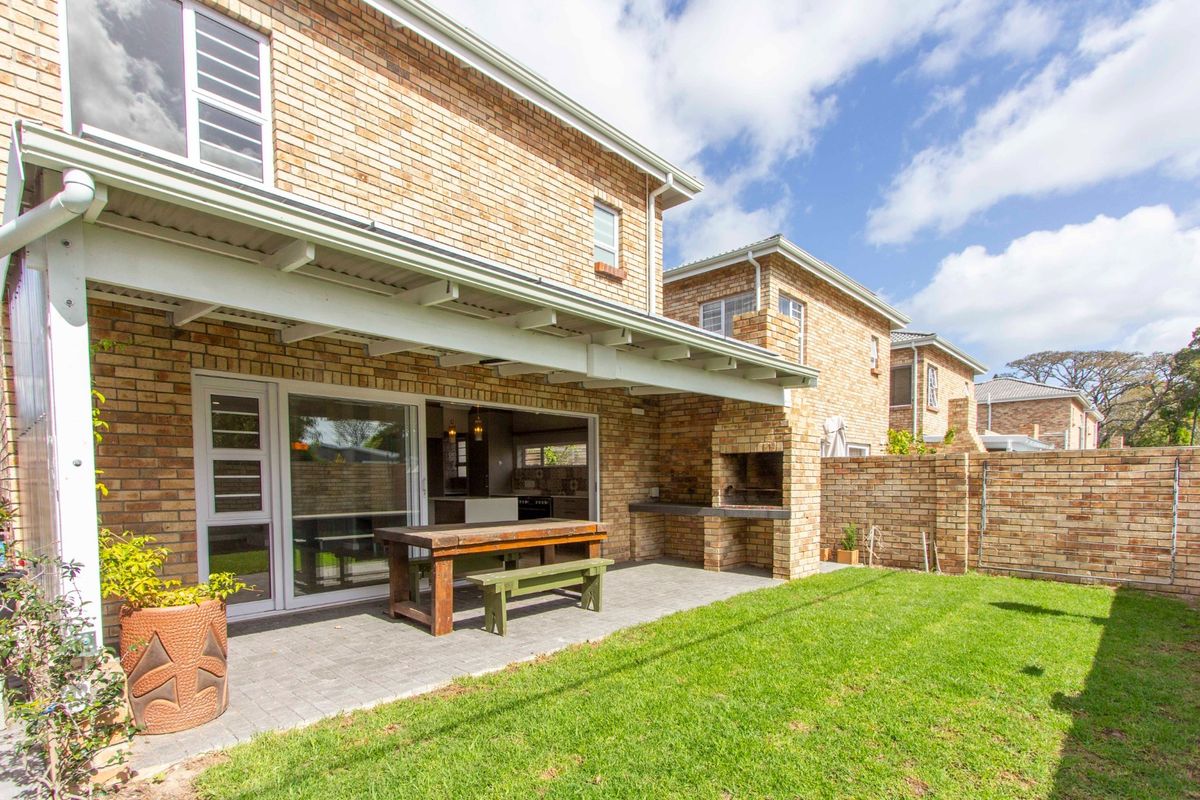 Rear view of the townhouse featuring a covered patio with a built-in braai, paved flooring, and access to the garden through sliding glass doors.