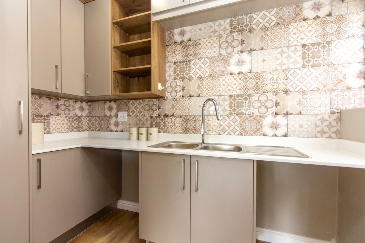 A modern, well-maintained kitchen area featuring neutral cabinetry, a double stainless steel sink, and decorative patterned tile splashbacks.