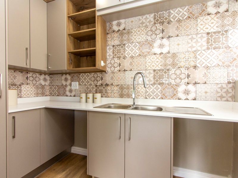 A modern, well-maintained kitchen area featuring neutral cabinetry, a double stainless steel sink, and decorative patterned tile splashbacks.