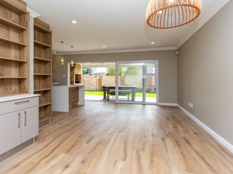 Spacious open-plan living area featuring modern laminate flooring, built-in cabinetry, and seamless access to the outdoor patio through large sliding glass doors.