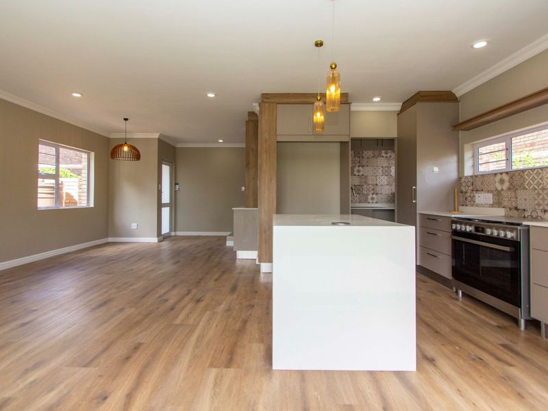 Spacious open-plan living and kitchen area featuring modern cabinetry, a central island, patterned tile backsplash, and durable laminate flooring throughout.