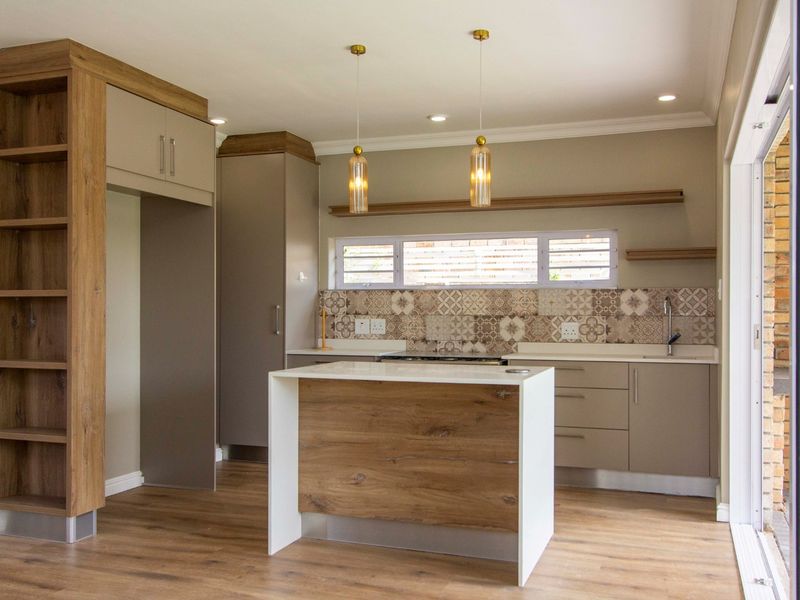 Modern kitchen featuring wood-tone cabinetry, a central island with stone countertop, patterned tile backsplash, and direct access to the outdoor area via sliding doors.