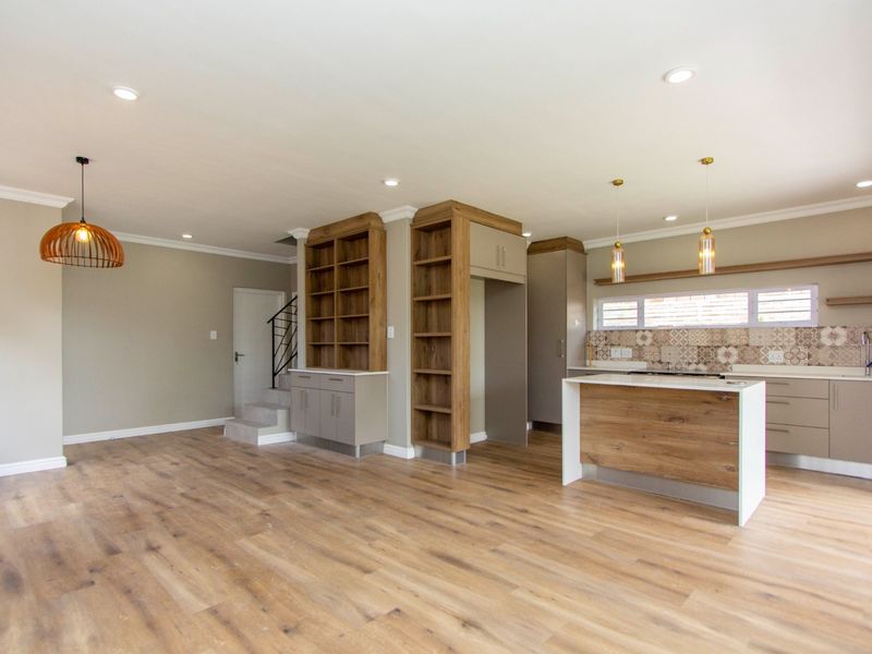 Modern open-plan living and kitchen area featuring wood-look laminate flooring, custom built-in cabinetry, a kitchen island, and stylish patterned tile backsplash.