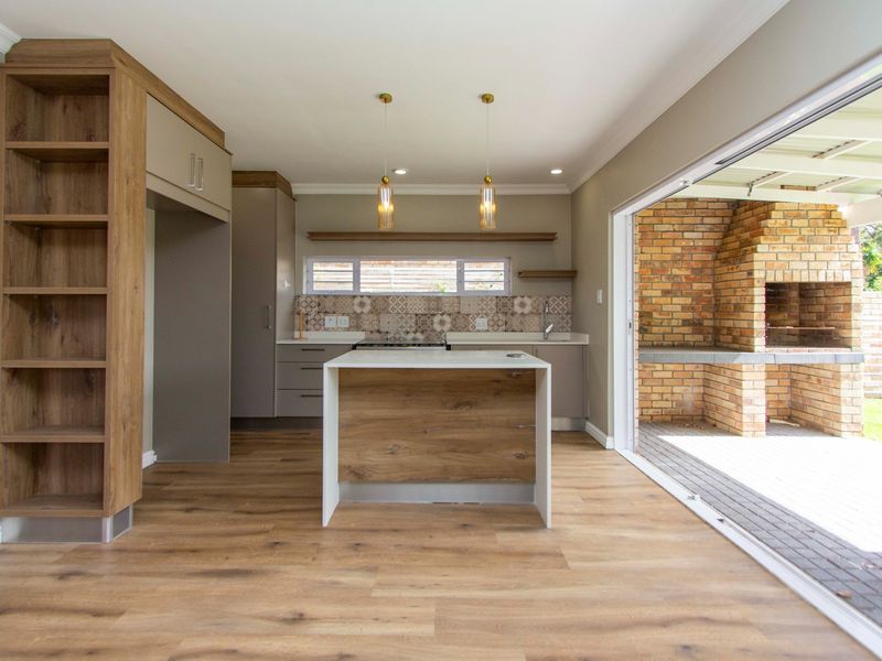 Modern open-plan kitchen featuring a central island, sleek cabinetry, and seamless flow to an outdoor patio area with a built-in brick braai.
