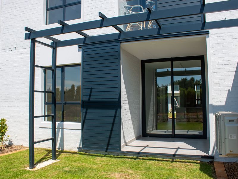 Rear exterior view of the apartment featuring a modern tiled patio, sliding glass doors, and a decorative timber pergola structure.