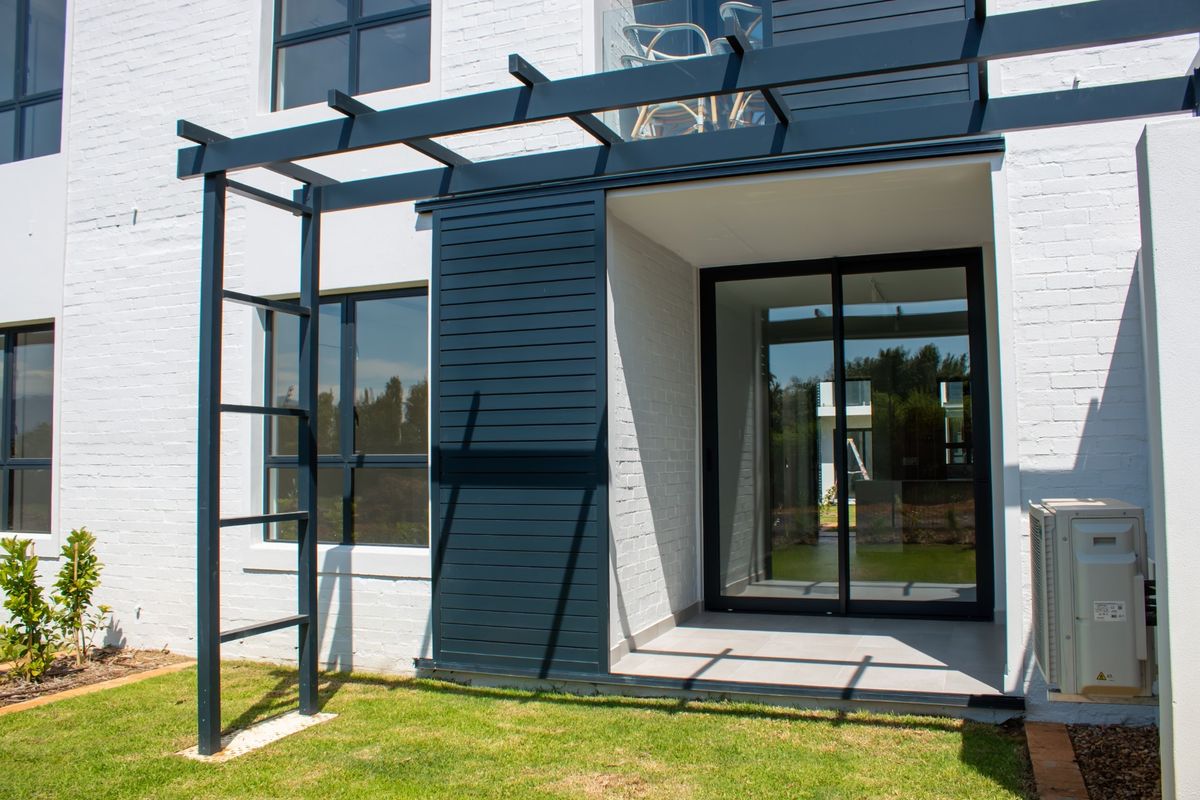 Rear exterior view of the apartment featuring a modern tiled patio, sliding glass doors, and a decorative timber pergola structure.