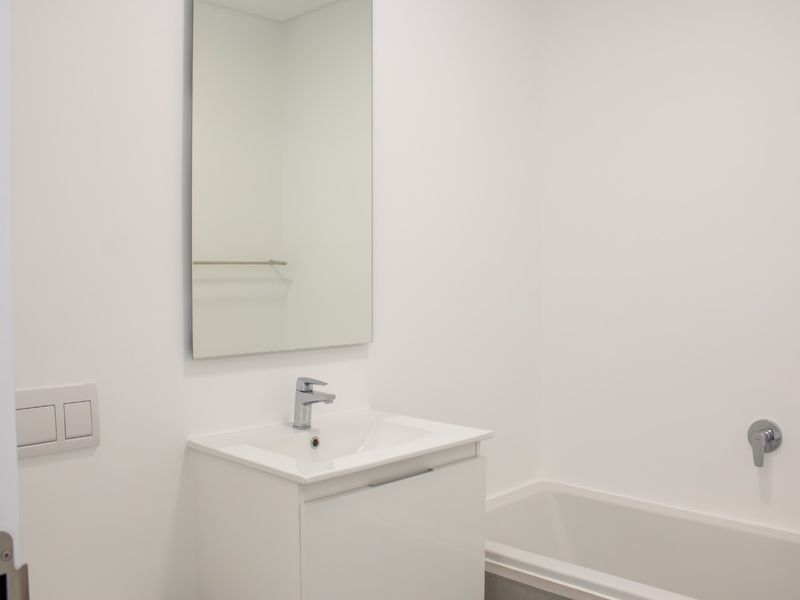A clean, modern bathroom featuring a white vanity with basin, wall-mounted mirror, and a bathtub with chrome fixtures.