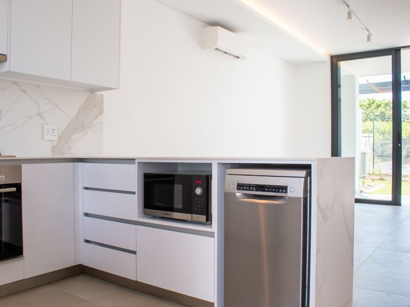 Modern kitchen featuring sleek white cabinetry, marble-look splashback, integrated appliances, and direct access to an outdoor area through sliding glass doors.
