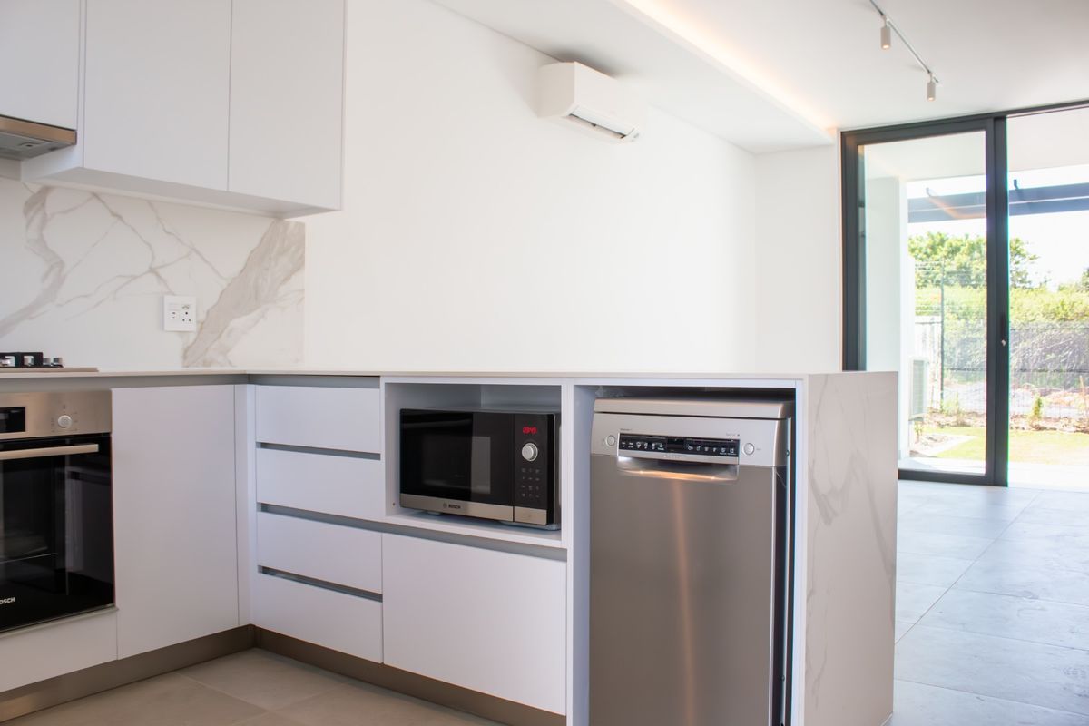 Modern kitchen featuring sleek white cabinetry, marble-look splashback, integrated appliances, and direct access to an outdoor area through sliding glass doors.