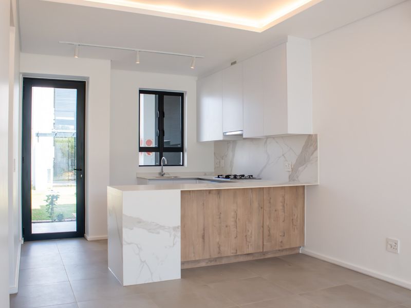 Modern kitchen featuring sleek white cabinetry, wood-grain accents, marble-look splashback, gas hob, and integrated lighting, offering a clean and contemporary aesthetic.
