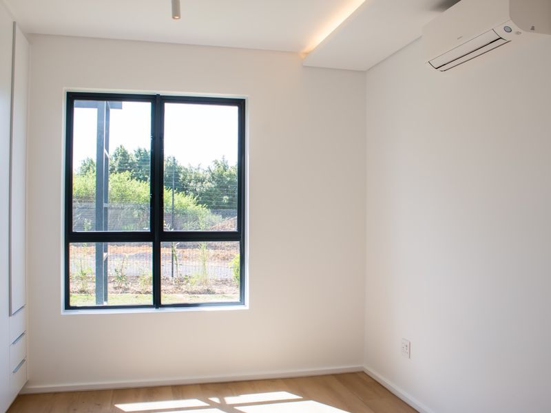 A bright, modern, and empty bedroom featuring built-in cupboards, laminate flooring, and a wall-mounted air conditioning unit.