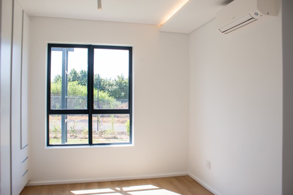 A bright, modern, and empty bedroom featuring built-in cupboards, laminate flooring, and a wall-mounted air conditioning unit.