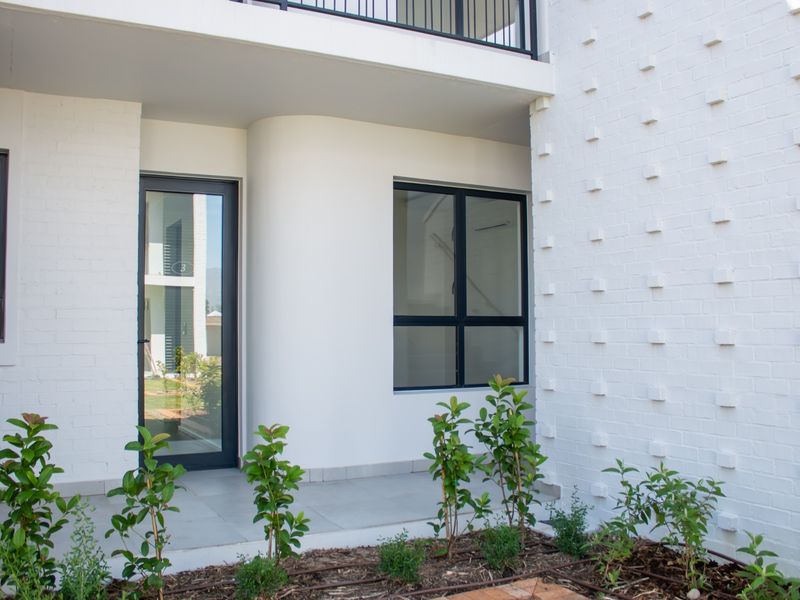 Modern apartment entrance featuring a clean white painted brick facade, dark aluminium window frames, and a tiled porch area.