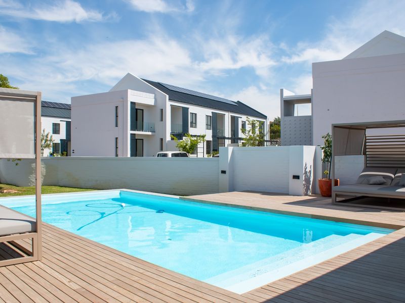 A well-maintained swimming pool area featuring timber decking and a clean boundary wall, set within a modern apartment complex.