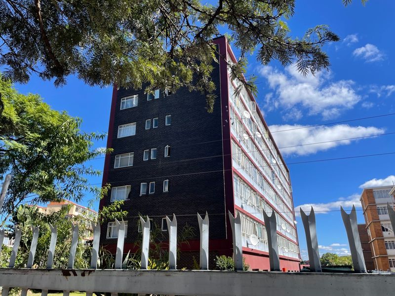 Exterior view of a multi-story apartment building featuring a dark brick facade and metal security fencing.
